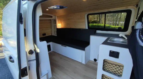 Interior de una Volkswagen T5 camperizada con asientos, cama, fregadero y armarios. Lista para viajar.