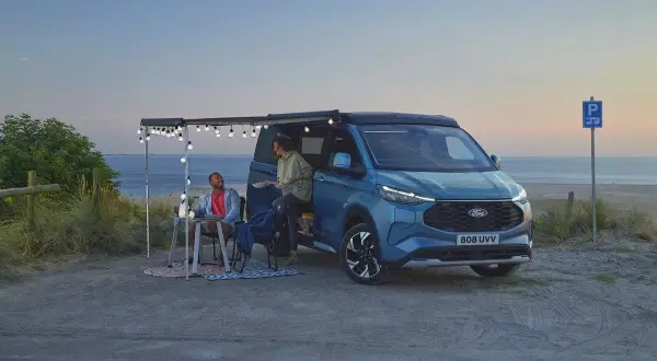 Pareja disfrutando en una playa con una camper hibrida enchufable azul, con toldo y luces.