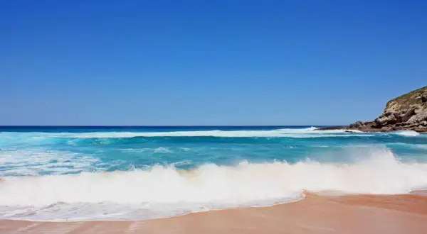 Olas rompiendo en una playa de arena dorada, ideal para saber donde hacer snorkel en Cantabria. Cielo azul intenso.
