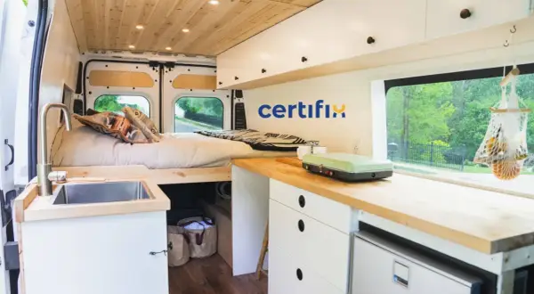 Interior de caravana con cama, fregadero y cocina. Muebles de madera y blancos, ideales para fabricantes de muebles para caravanas.