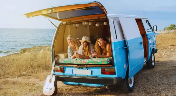 Tres amigas disfrutan de la vida en su furgoneta camperizada junto al mar. Inspiración para saber como camperizar una furgoneta.