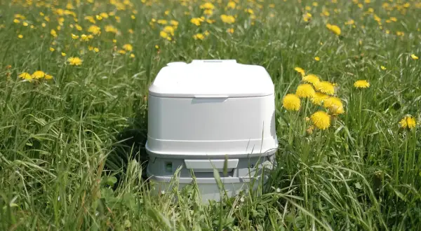 Un inodoro portátil blanco en un campo de flores amarillas. Así es como funciona un poti, una solución práctica para la naturaleza.