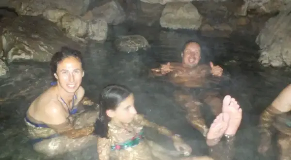 Familia disfrutando de las pozas termales del río Deva, rodeados de rocas y agua cálida.