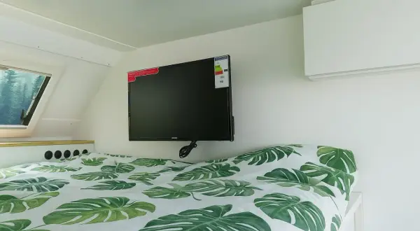 Cama con sábanas de hojas verdes y un televisor de consumo tv 50 pulgadas colgado en la pared.