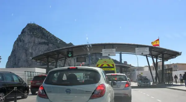 Fila de coches en la frontera de Gibraltar, con el Peñón al fondo. Señales indican dónde dove parcheggiare a Gibilterra.