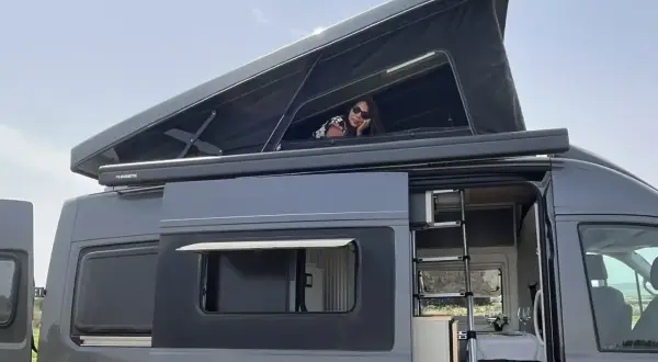 Mujer asomada en la cama elevada de una furgoneta camper. Las medidas de esta furgoneta man son perfectas para viajar.