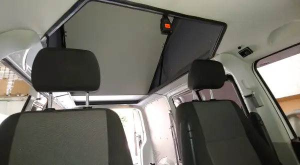 Interior de furgoneta con asientos delanteros y un techo elevable abierto, listo para la aventura.