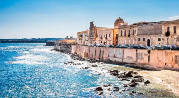 Costa de Siracusa, Sicilia, con edificios históricos y el mar azul brillante.