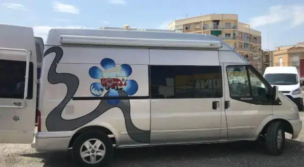 Furgoneta camperizada con motor Ford 2.2 TDCI 140 CV. Decoración de flor azul y carretera gris.