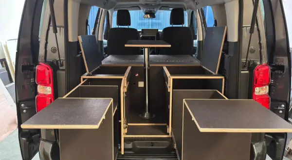 Soluciones de trucos almacenaje furgonetas camper: módulos de madera con compartimentos y mesa abatible para maximizar el espacio.