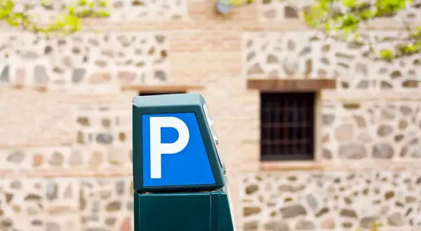 Parquímetro azul con letra P blanca, señalando opciones de altstadt Marbella parken. Edificio de piedra y ladrillo al fondo.