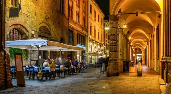 Noche en Bolonia, con gente cenando bajo toldos. Imagina cómo ir de Milán a Bolonia y disfrutar de esta escena.