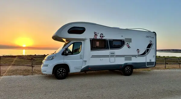 Autocaravana blanca aparcada junto al mar al atardecer. ¡La aventura de **Sicilia en autocaravana** comienza!