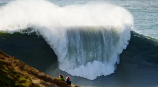 Dos personas observan desde un mirador las gigantescas olas de Nazaré, un espectáculo natural impresionante.