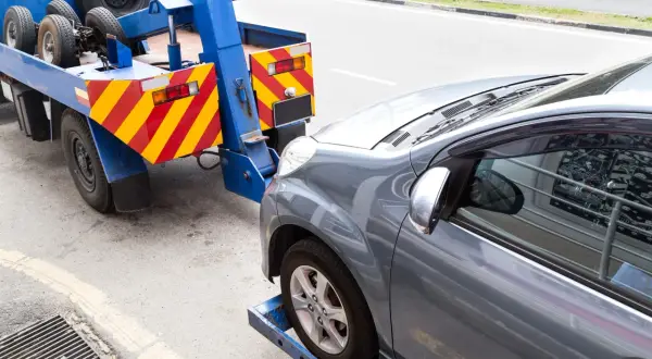 Grúa azul lista para transportar caravana. El coche gris está asegurado en la plataforma.