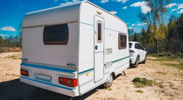 Caravana blanca lista para el transporte, aparcada junto a un coche en un día soleado.