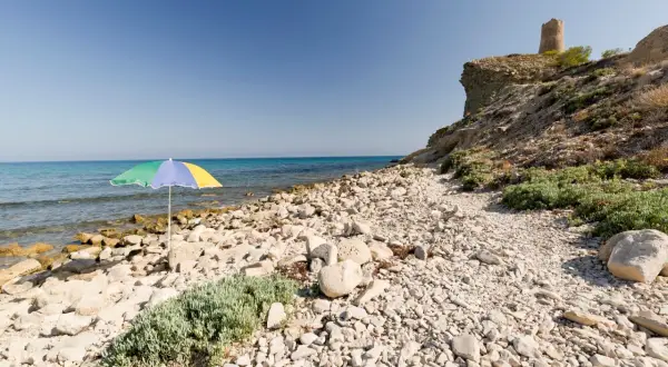 Sombrilla de colores en la playa de las covaticas, con mar turquesa y torre antigua en el acantilado.