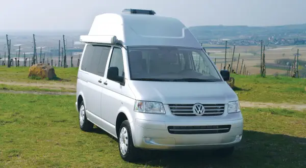Furgoneta Volkswagen Transporter T5 camperizada con techo elevable, aparcada en un prado con vistas a un valle.