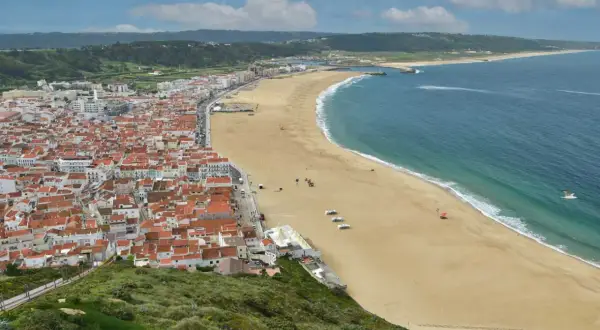 Vista aérea de Nazaré, Portugal, con su extensa playa dorada y el mar azul. Planifica tu viaje a Nazaré, Portugal, como llegar es fácil.