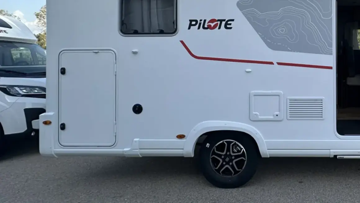 Autocaravanas con garaje, listas para la aventura. Detalle lateral de una autocaravana blanca con puerta de acceso y detalles gráficos.