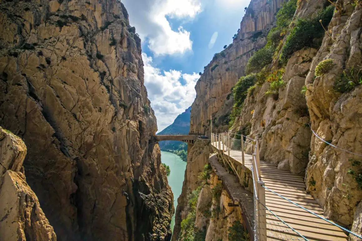 El sendero del koningspad en España, un camino de madera suspendido sobre un desfiladero con un río turquesa abajo.