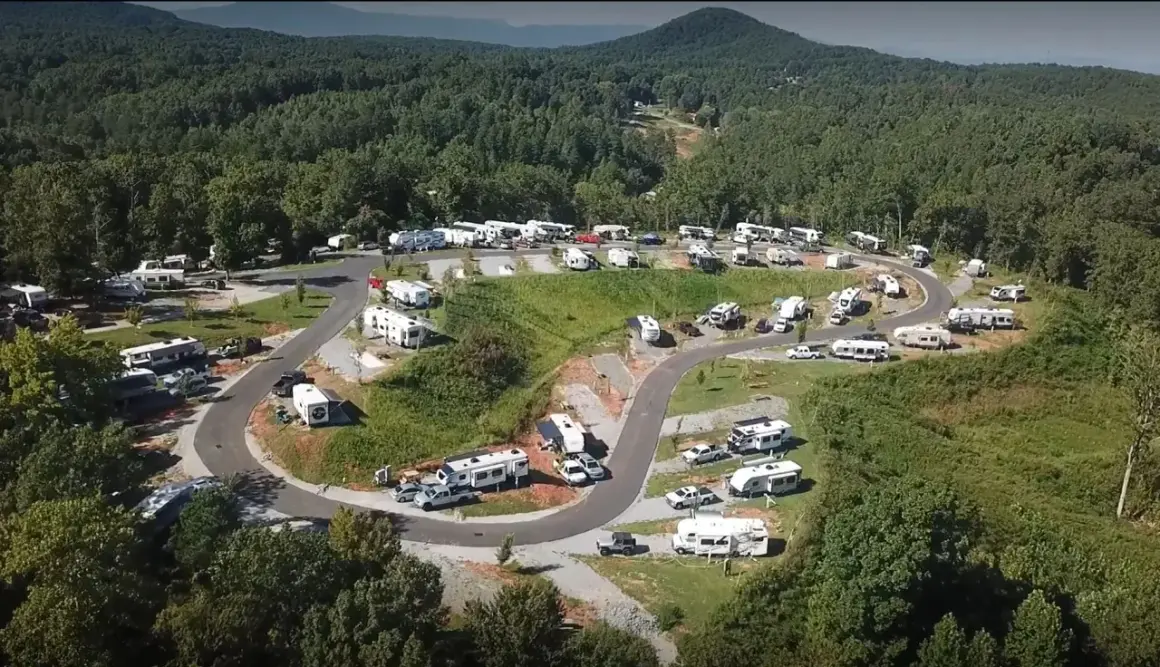 Vista aérea de un camping con muchas autocaravanas y remolques estacionados en un terreno montañoso. Ideal para quienes buscan camping.