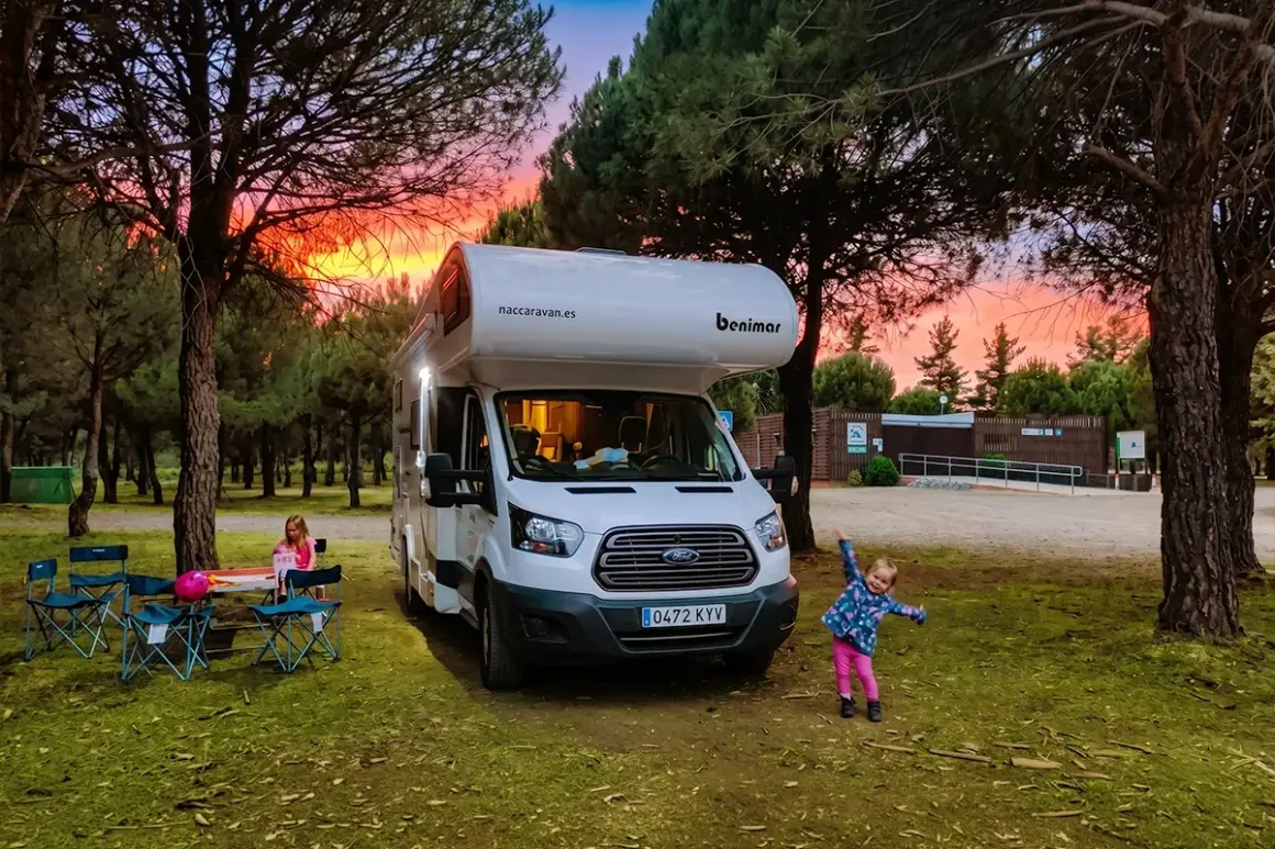 Autocaravana Benimar en un camping al atardecer. Niños jugando y disfrutando.