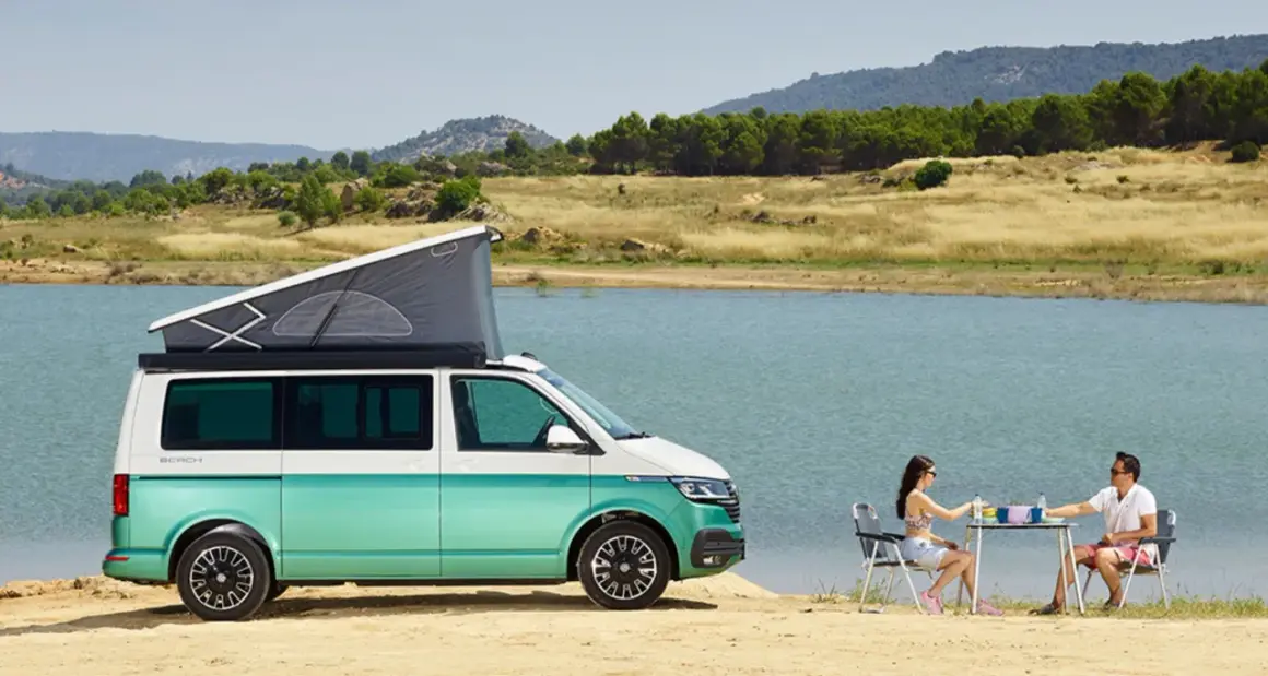 Volkswagen California con baño, lista para una escapada junto al lago. Pareja disfruta de un picnic al aire libre.