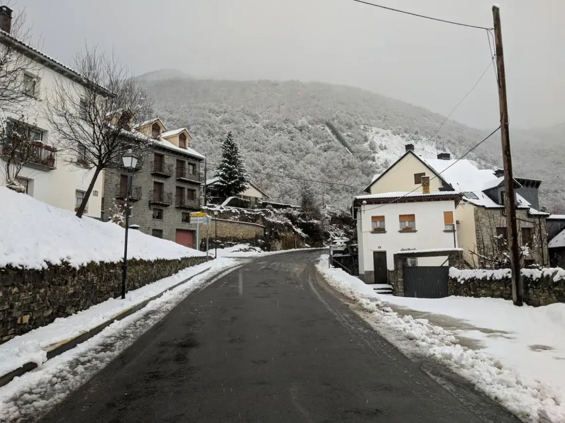 Un pueblo nevado, ideal para un fin de semana en Jaca. Casas de piedra y tejados blancos bajo un cielo gris.
