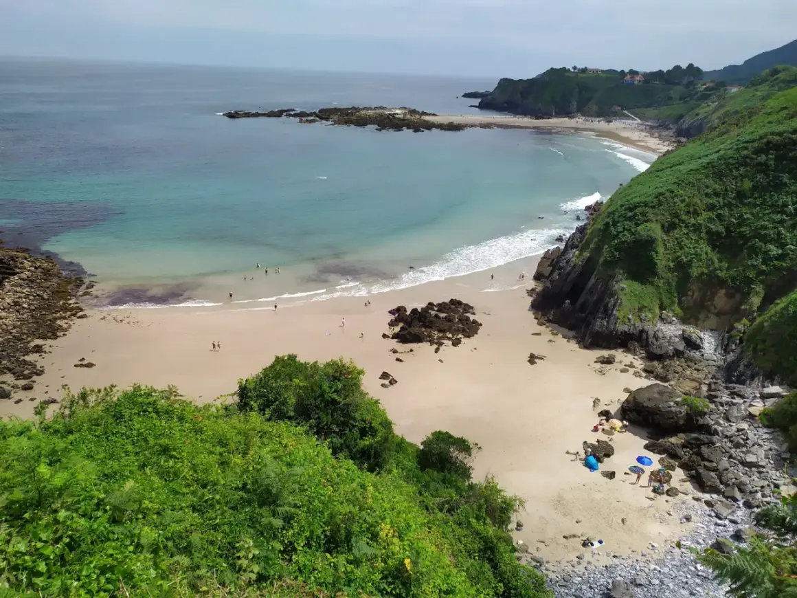 Vista aérea de la playa de Aramal, con arena dorada, aguas turquesas y gente disfrutando del sol y el mar.