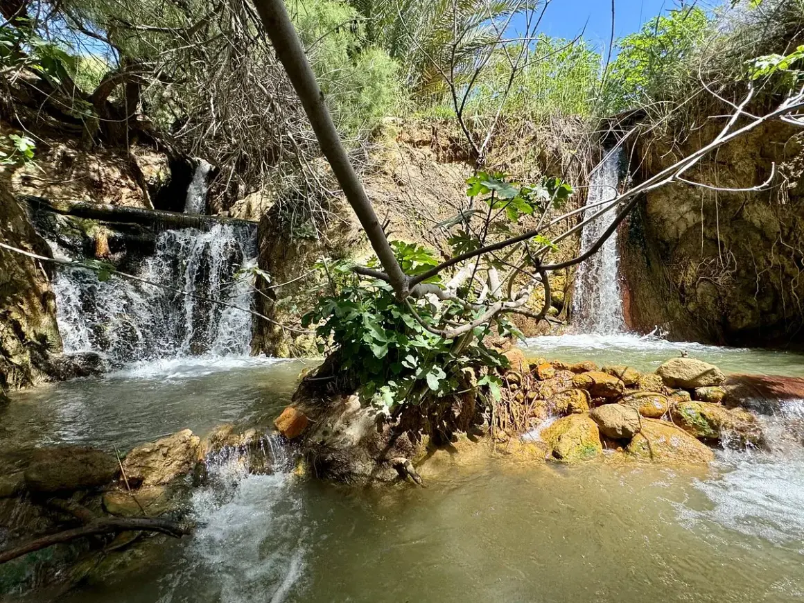 Cascada natural en las aguas termales Santa Fe, con rocas anaranjadas y vegetación exuberante.