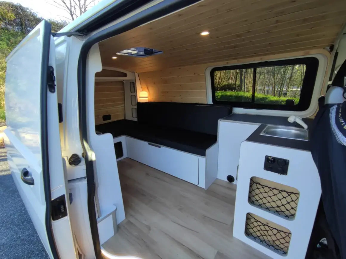Interior de una Volkswagen T5 camperizada con asientos, cama, fregadero y armarios. Lista para viajar.