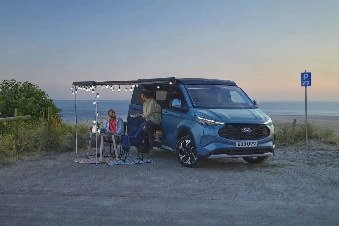 Pareja disfrutando en una playa con una camper hibrida enchufable azul, con toldo y luces.