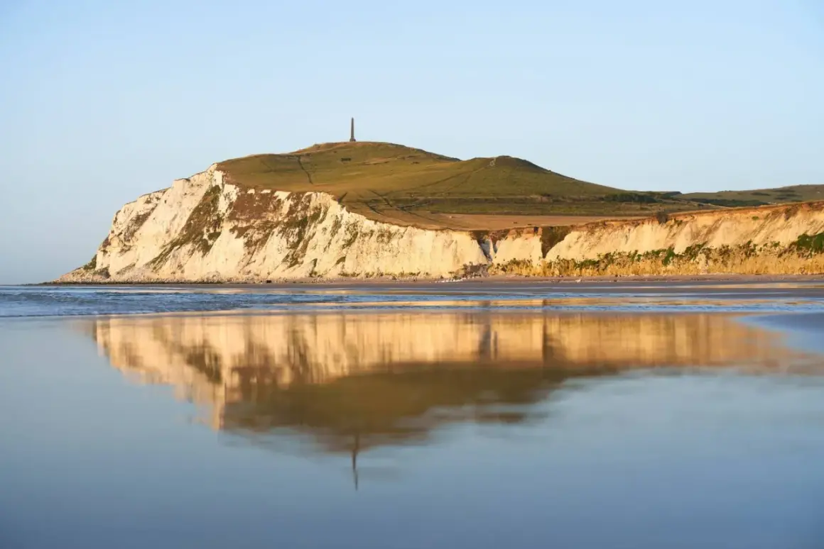 Acantilados blancos y verdes en Cap Blanc Nez, reflejados en el mar tranquilo.