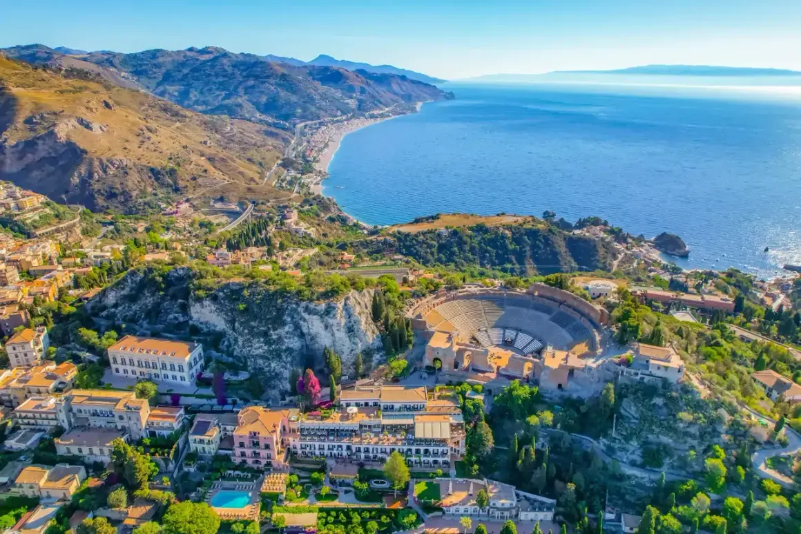 Vista aérea del antiguo teatro griego de Taormina, uno de los lugares más bonitos de Sicilia, con el mar azul y la costa al fondo.