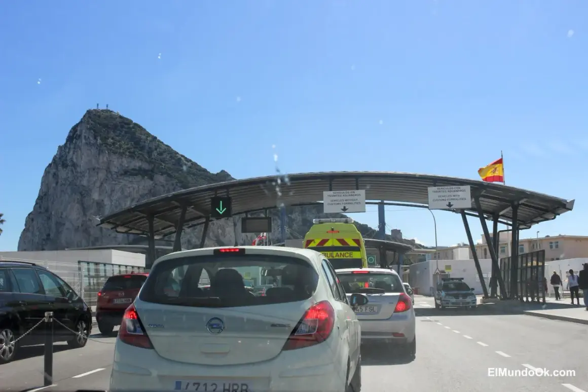 Fila de coches en la frontera de Gibraltar, con el Peñón al fondo. Señales indican dónde dove parcheggiare a Gibilterra.