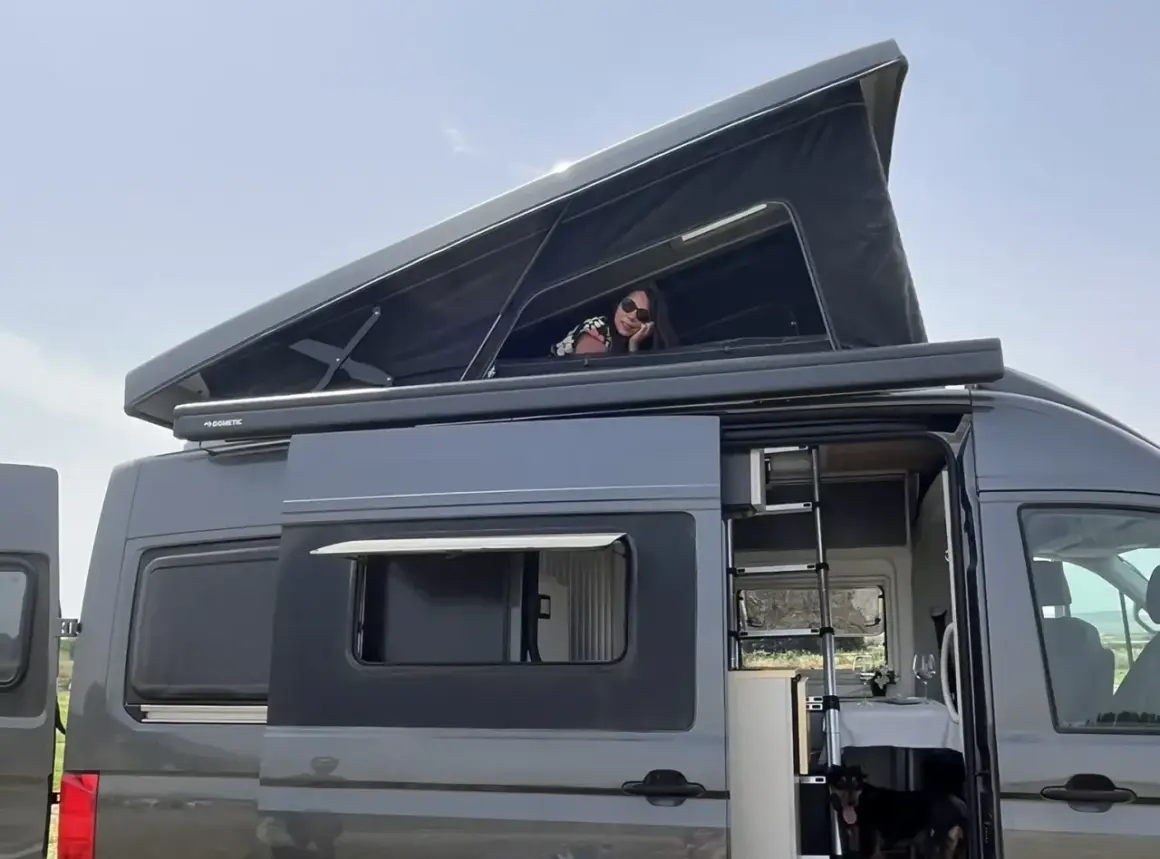 Mujer asomada en la cama elevada de una furgoneta camper. Las medidas de esta furgoneta man son perfectas para viajar.