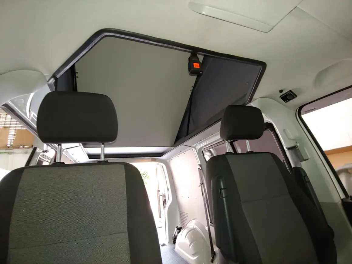 Interior de furgoneta con asientos delanteros y un techo elevable abierto, listo para la aventura.