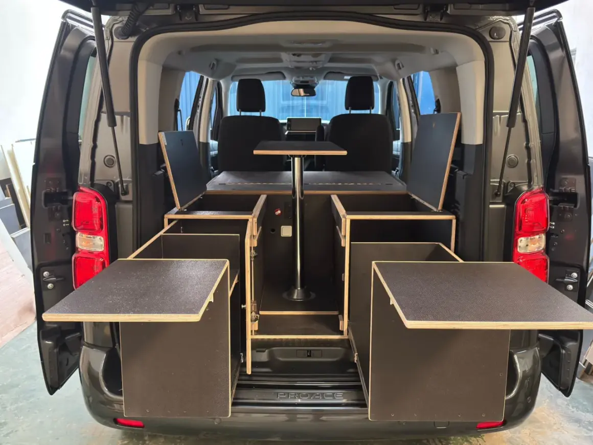 Soluciones de trucos almacenaje furgonetas camper: módulos de madera con compartimentos y mesa abatible para maximizar el espacio.