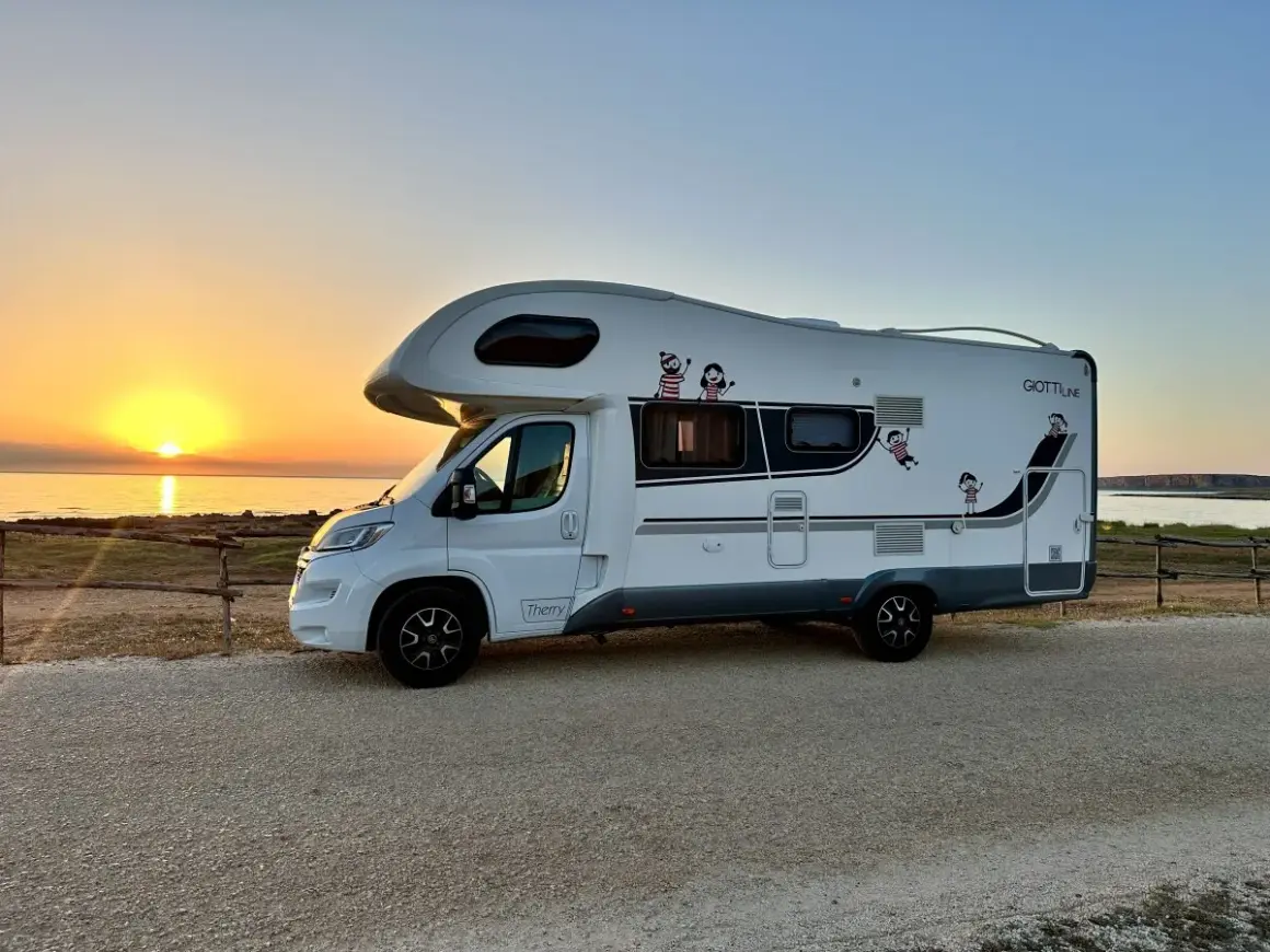 Autocaravana blanca aparcada junto al mar al atardecer. ¡La aventura de **Sicilia en autocaravana** comienza!