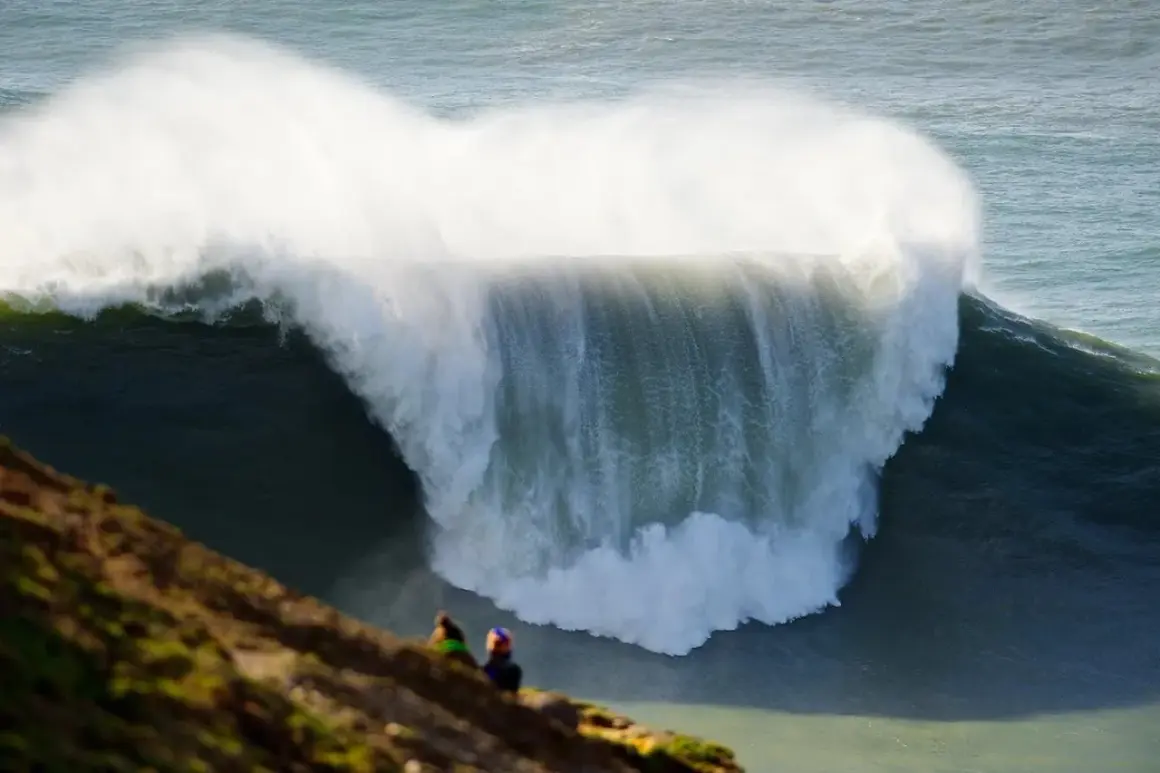 Dos personas observan desde un mirador las gigantescas olas de Nazaré, un espectáculo natural impresionante.