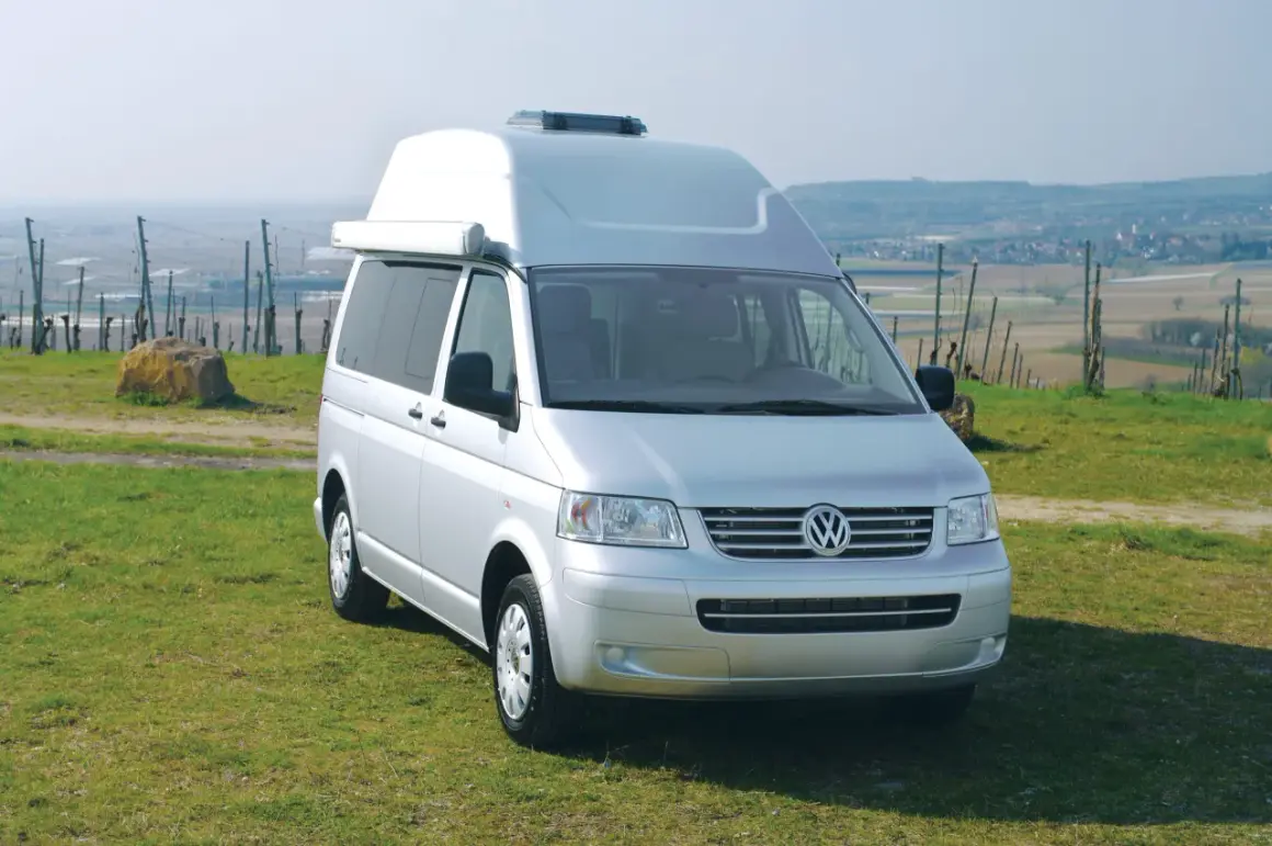 Furgoneta Volkswagen Transporter T5 camperizada con techo elevable, aparcada en un prado con vistas a un valle.