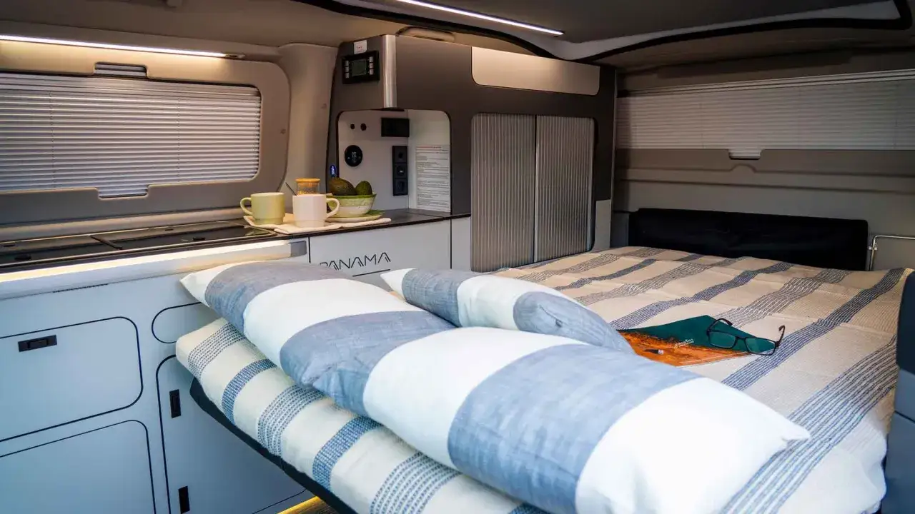 Interior de una camper hibrida enchufable con cama, cocina y armarios. Perfecta para aventuras sostenibles.