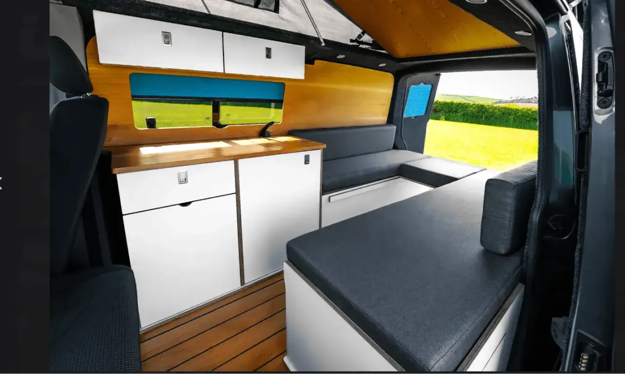 Interior de volkswagen t5 camper con cama, cocina y armarios.