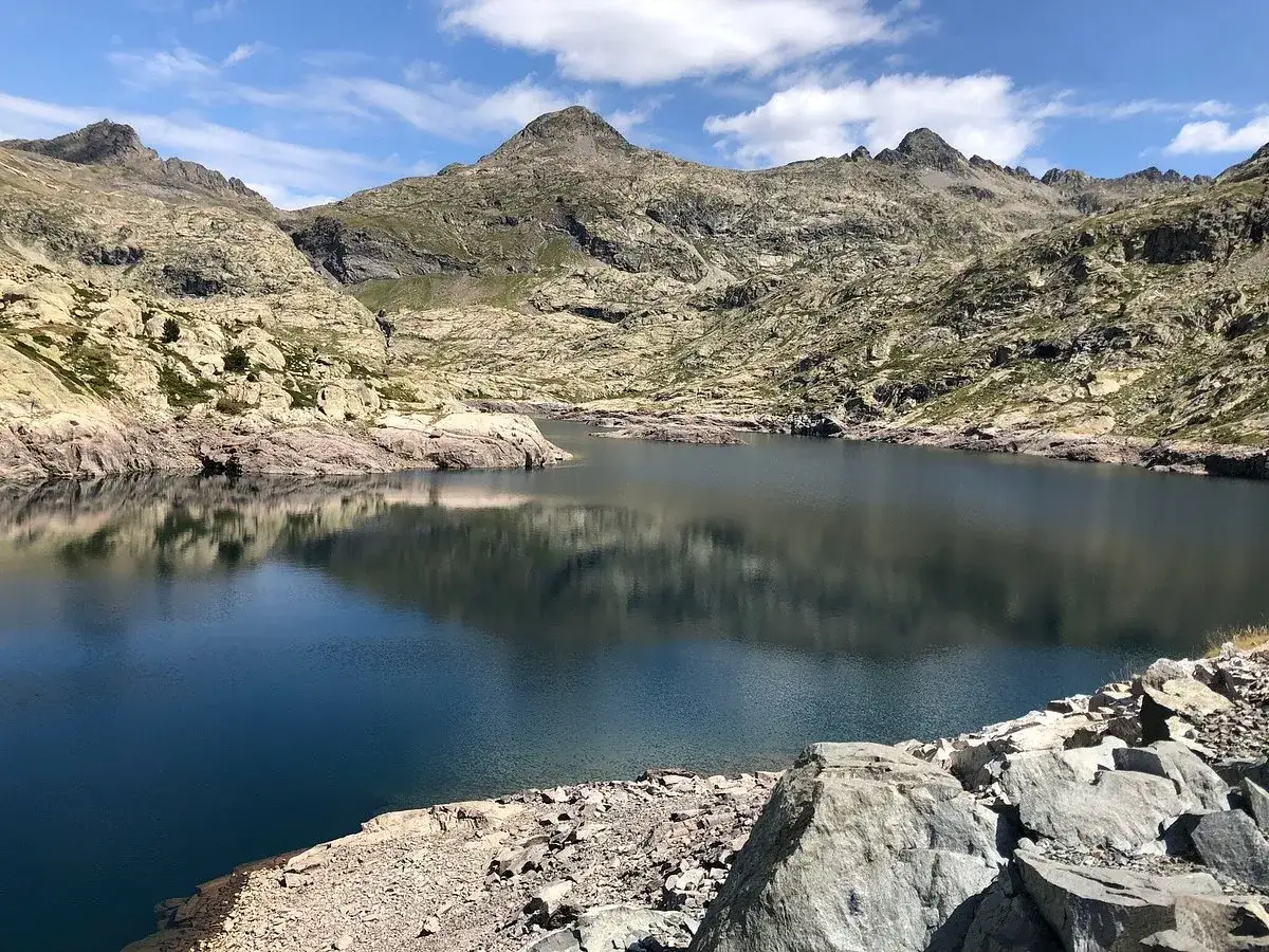 Reflejo perfecto de las monta&ntilde;as en los ibones de Bachima&ntilde;a. Un paisaje sereno y majestuoso bajo un cielo azul con nubes algodonosas.