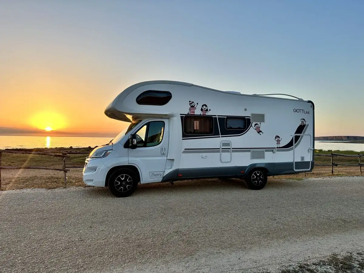 Autocaravana blanca aparcada en la costa, disfrutando de un atardecer espectacular. ¡La aventura de Sicilia en autocaravana comienza!
