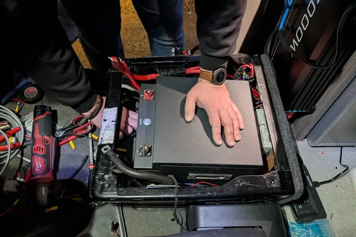 Instalación de una batería AGM en un vehículo. Se ven cables, herramientas y un inversor.