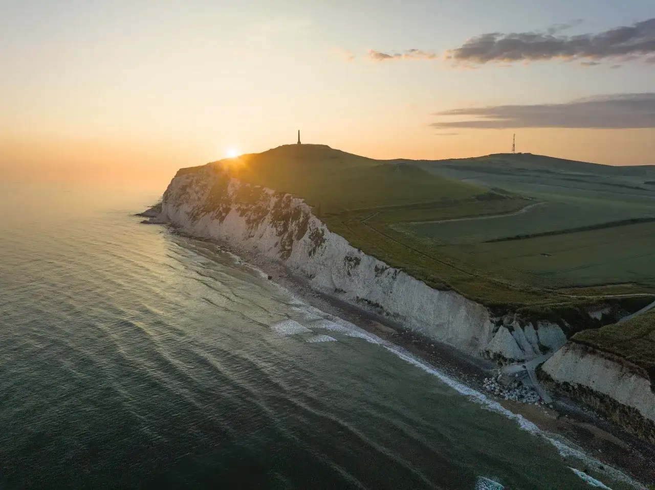 Amanecer dorado sobre los acantilados blancos de Cap Blanc Nez, con el mar ondulante y colinas verdes.
