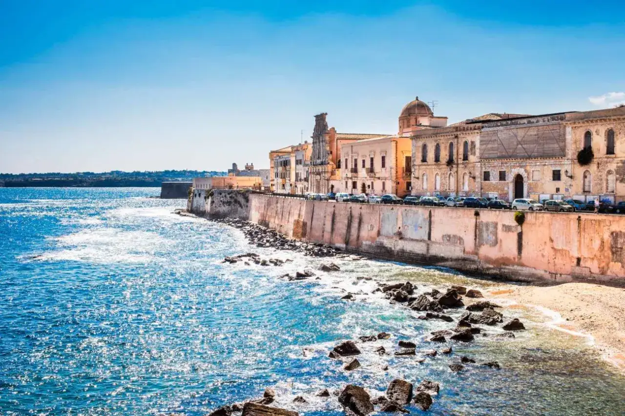 Costa de Siracusa, Sicilia, con edificios hist&oacute;ricos y el mar azul brillante.