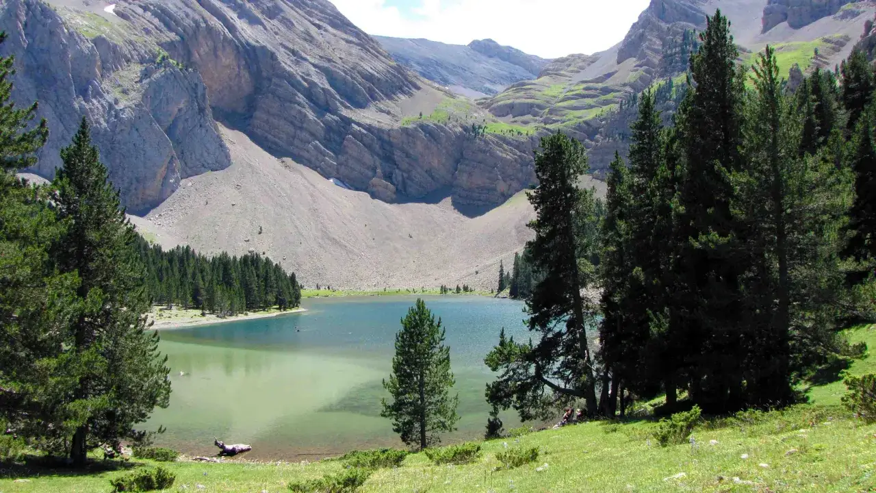 Paisaje alpino con un lago turquesa, rodeado de pinos y monta&ntilde;as escarpadas. La ruta Ibon de Plan ofrece vistas espectaculares.